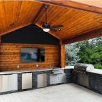 Outdoor kitchen under a wooden pergola with a ceiling fan