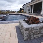 Outdoor patio with a modern rectangular pool, stone fire pit in the foreground