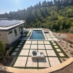 Modern house with solar panels, overlooking a sleek pool and geometric stone patio