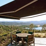 awning covering patio with table and chairs, overlooking a calm lake