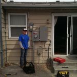 electrician standing beside an installed electrical box on a house's exterior wall