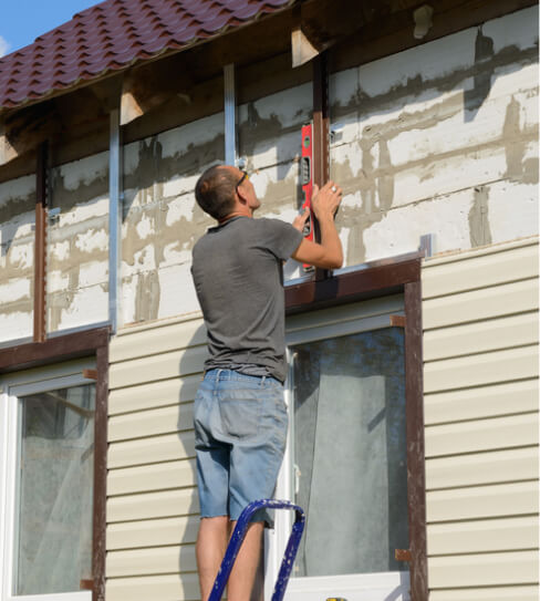 Worker using level bar on outside wall of a house