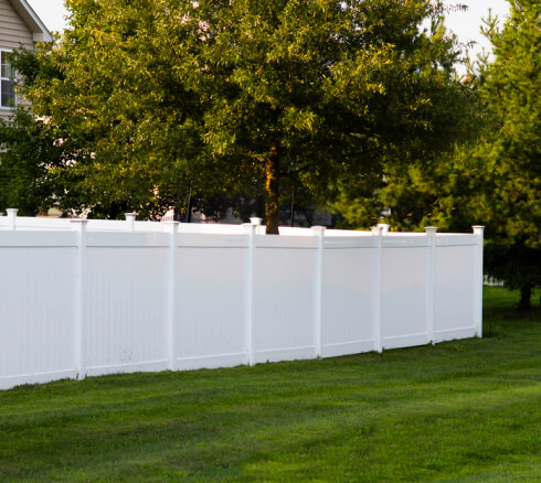 Solid white vinyl fence on a backyard with lots of trees