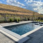 A serene backyard pool with clear water, surrounded by a stone patio