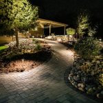 paved walkway to a home surrounded by landscape at night