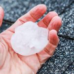 A person holding a large hailstone that hit a roof