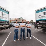 three men standing behind two Checkmate Moving and Storage trucks