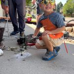young boy with glasses and cap holding a concrete leveling tool